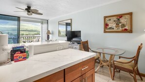 A modern kitchen with a marble countertop, wooden cabinets, a ceiling fan, and a large window offering a view of the outdoors. - Lahaina Shores #532 Studio Bedroom Condo by RedAwning (Lahaina)