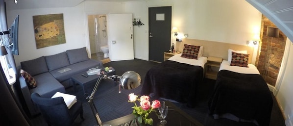 A hotel room with a sofa, two beds, a desk, a mirror, and a vase with flowers.