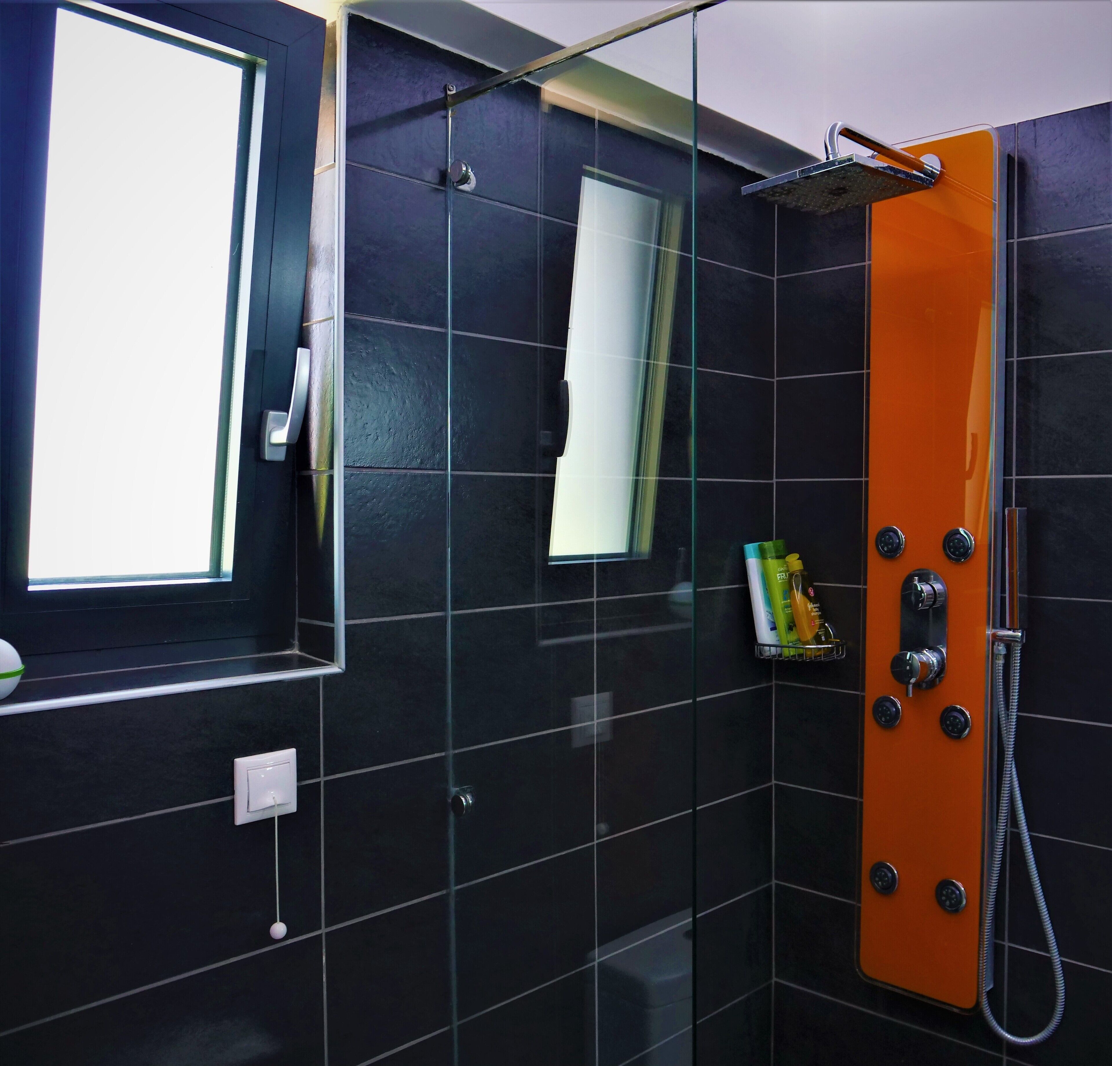 A modern bathroom with black tiles, a glass shower enclosure, and a window.