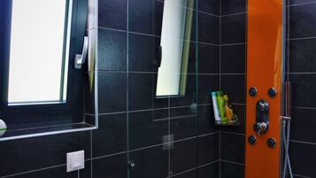 A modern bathroom with black tiles, a glass shower enclosure, and a window.