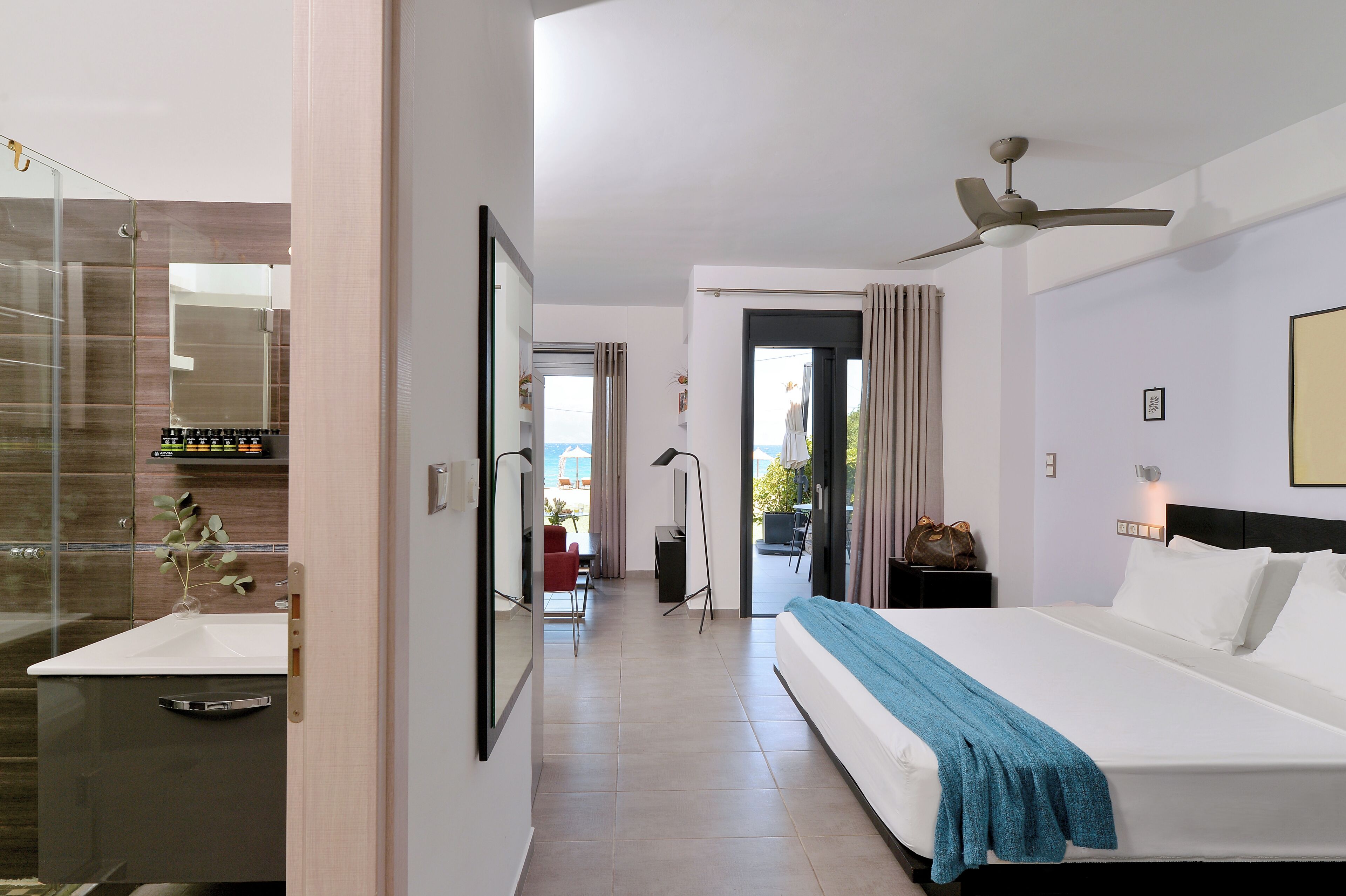 A hotel room with a bed, bedside table, nightstand, and a view through an open door to a balcony.