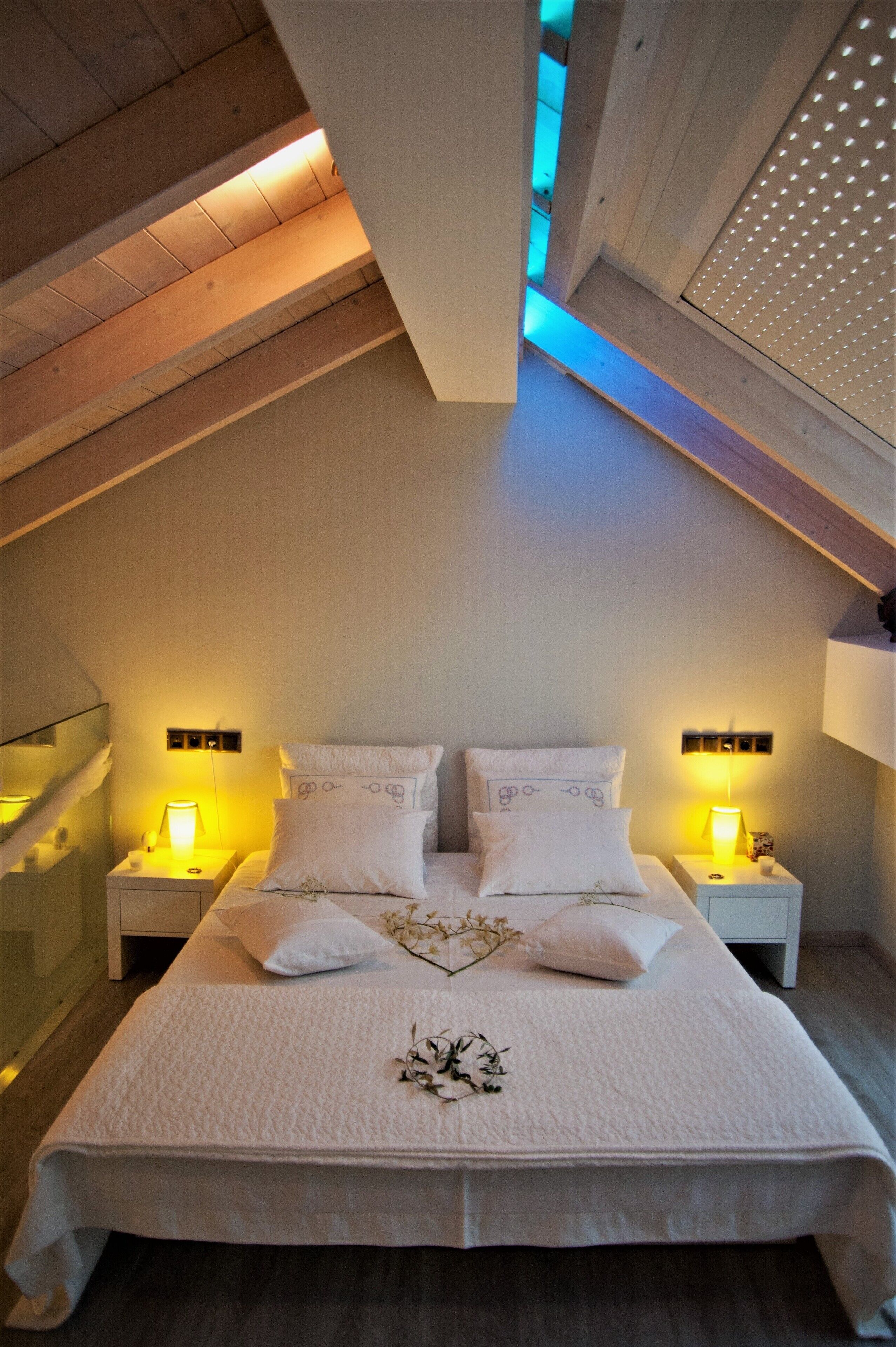 A bedroom with a large bed, two bedside tables with lamps, and a sloped ceiling with wooden beams.