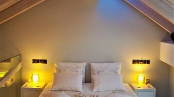 A bedroom with a large bed, two bedside tables with lamps, and a sloped ceiling with wooden beams.