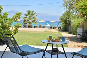 Un patio con mobiliario exterior, una mesa con alimentos para el desayuno y vistas a la playa y al océano.