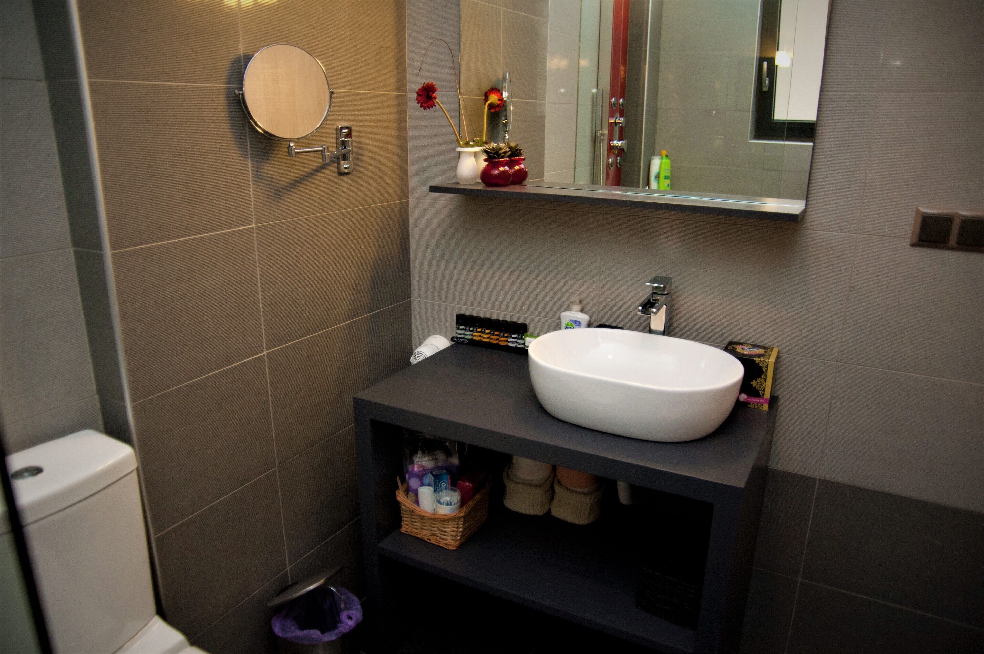 Een moderne badkamer met een ronde spiegel, een witte wastafel en een klein plankje met toiletartikelen.
