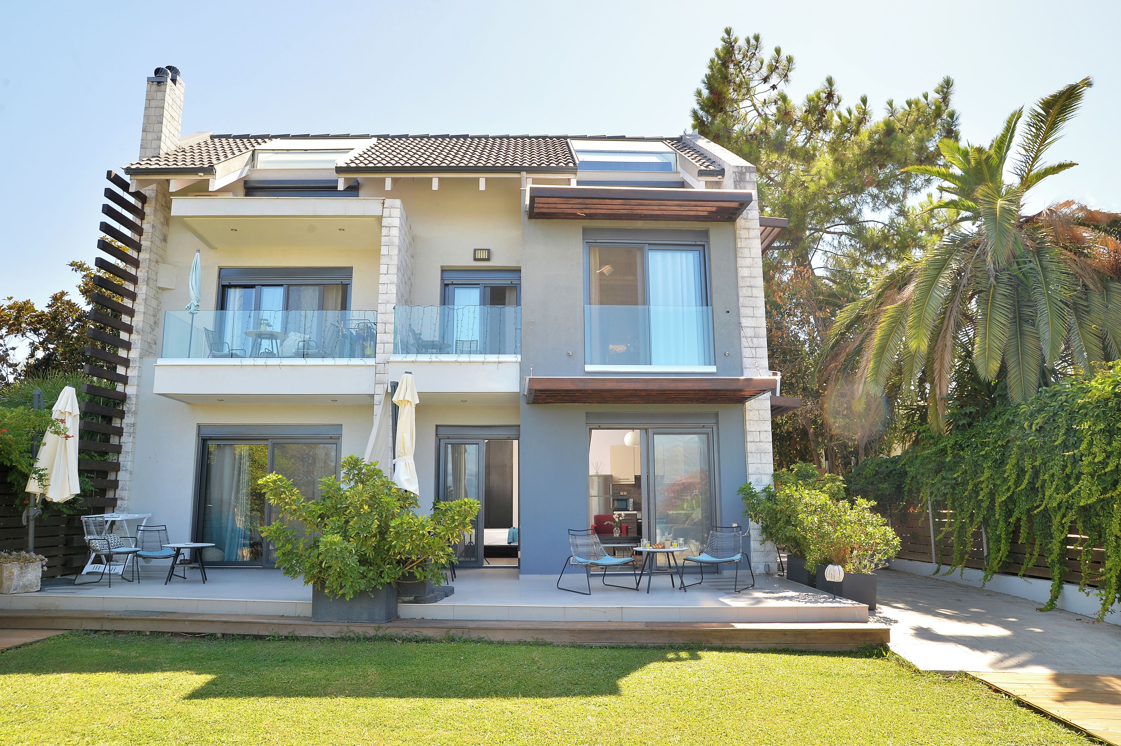A two-story house with a balcony, a patio with outdoor furniture, and a well-maintained garden.