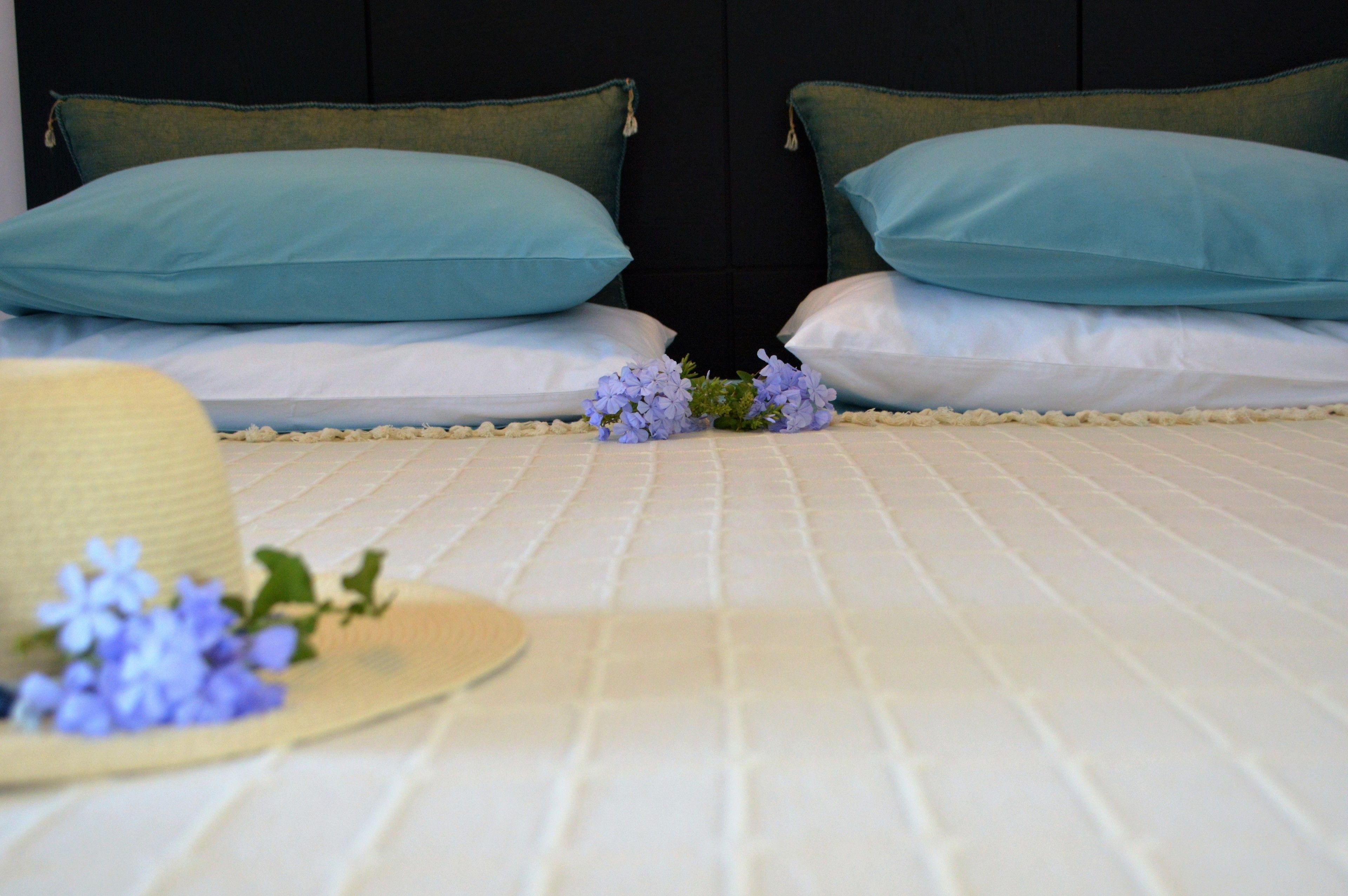 A neatly made bed with two pillows, a hat, and a small bouquet of flowers on the bed.