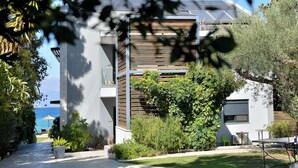 A modern building with a balcony, a view of the sea, and a garden area with plants and outdoor furniture.