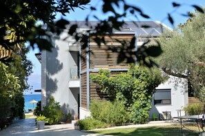 Un edificio moderno con balcón, vistas al mar y un jardín con plantas y mobiliario exterior.