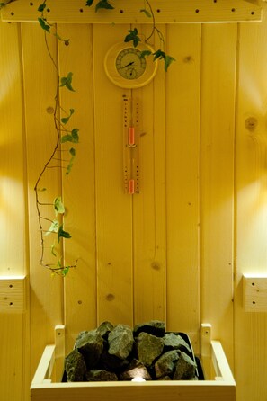A wooden sauna with a thermometer, a clock, and a rock-filled basin. - Seacret Apartments (Aigialeia)