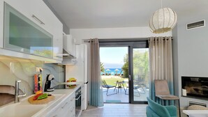 Cozinha moderna com uma janela ampla, área de refeições com mesa e cadeiras, e vista para a praia.