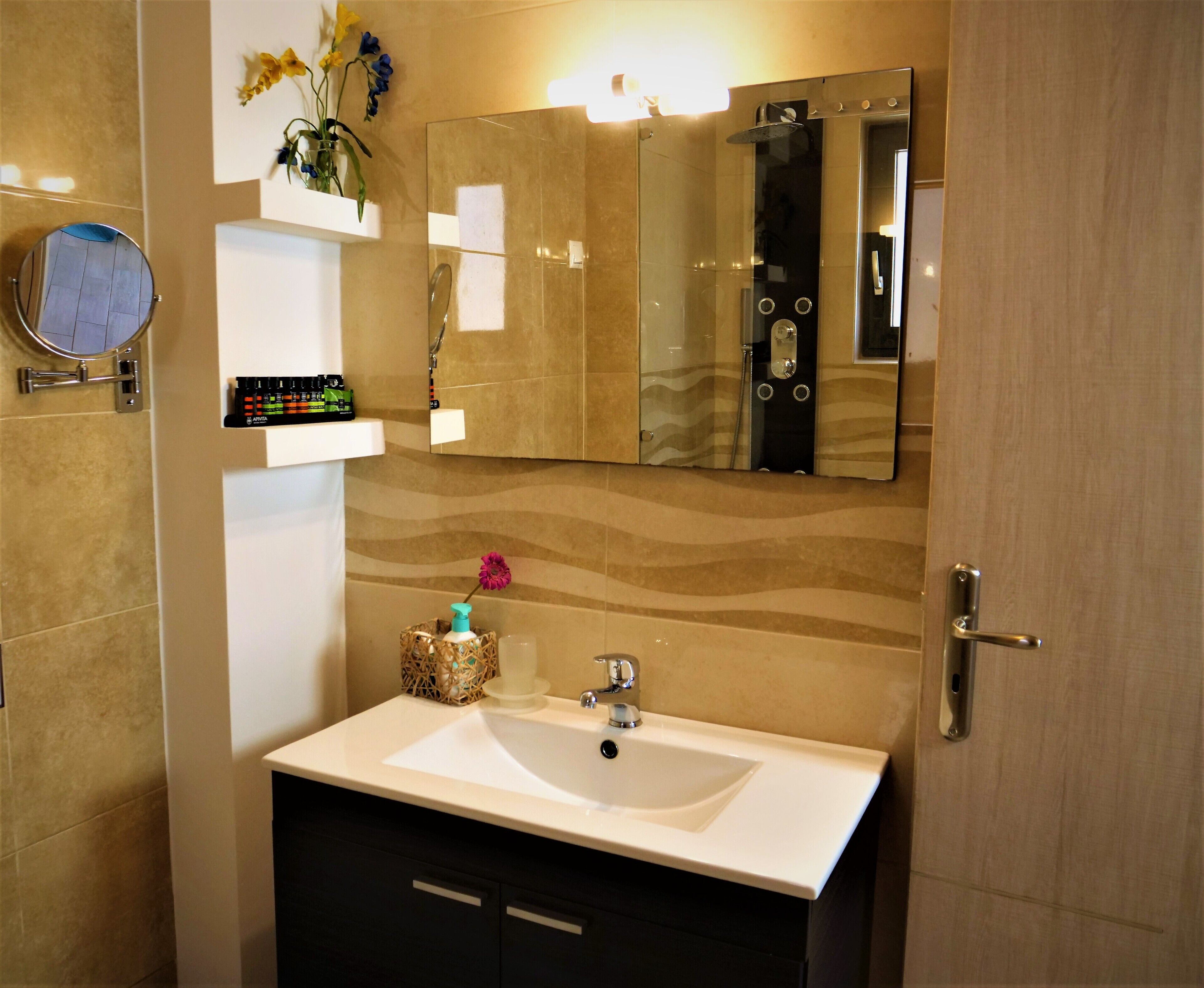 A bathroom with a white sink, dark cabinets, a mirror, and a shower area.