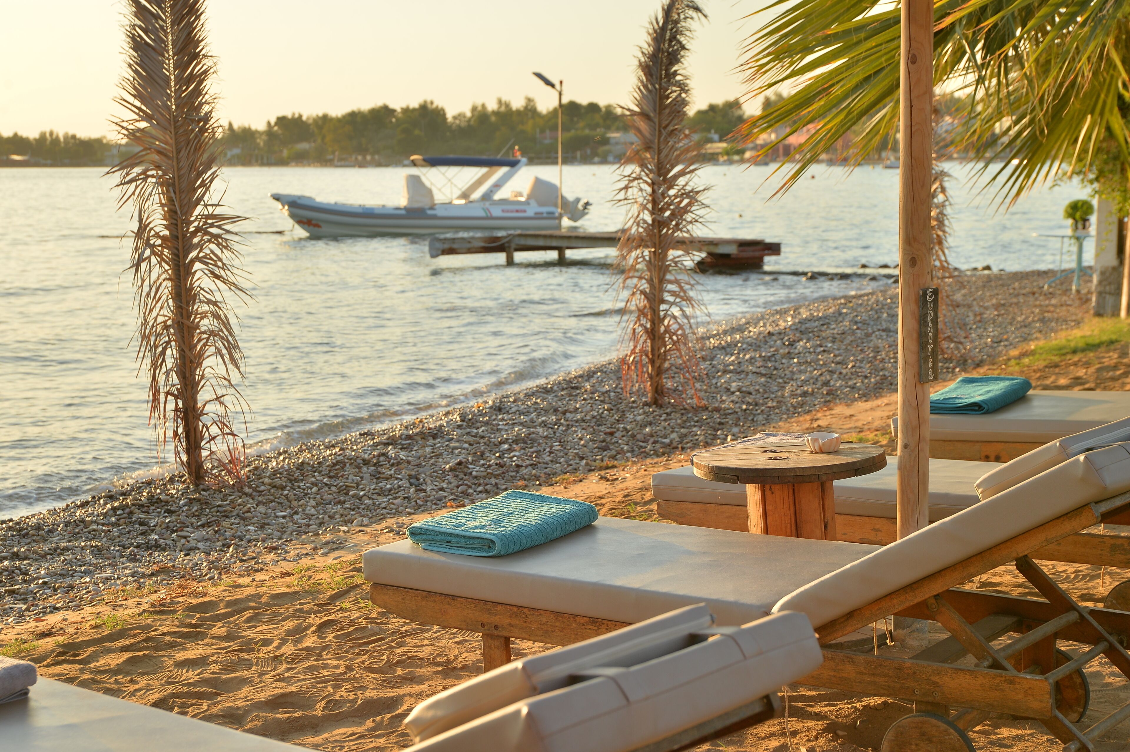 Un entorno frente a la playa con sillas de descanso, una mesa pequeña y un barco al fondo.