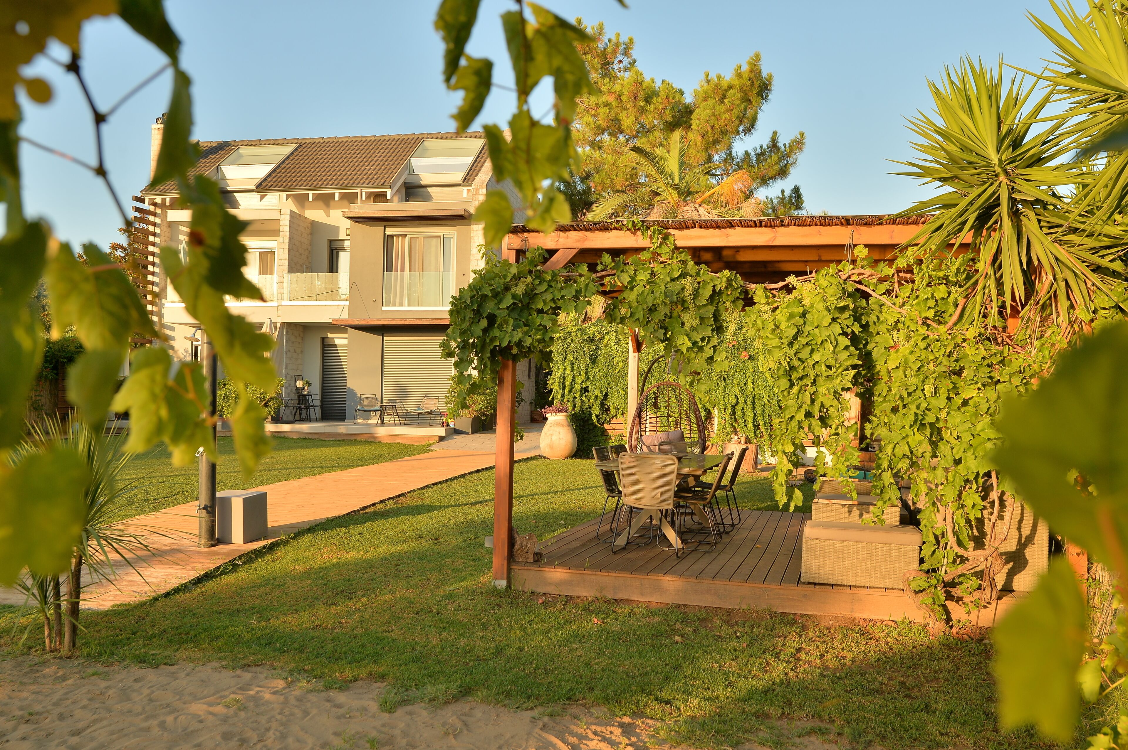 Une terrasse avec des meubles d’extérieur, une pergola couverte de plantes grimpantes et un bâtiment en arrière-plan.