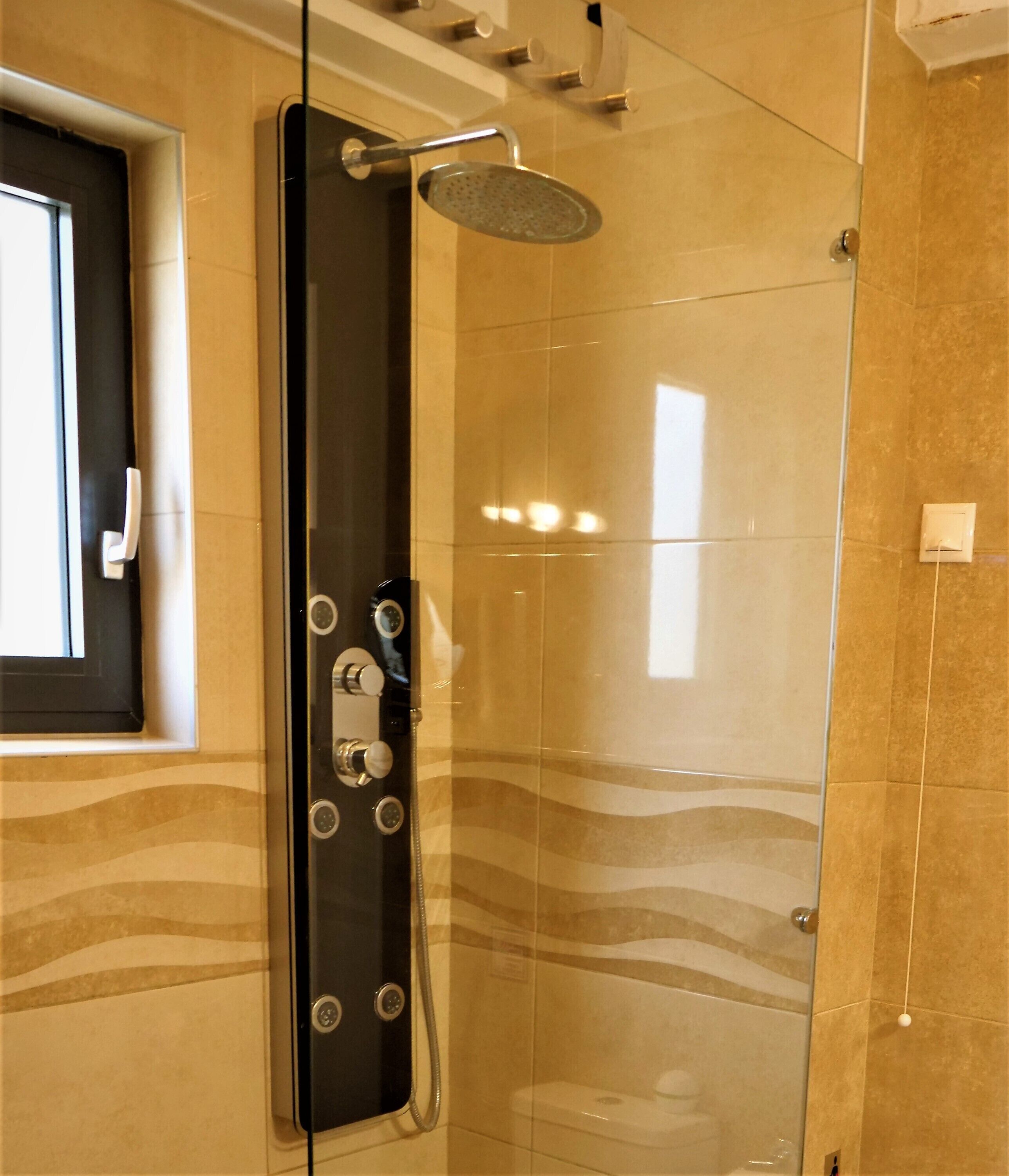 A modern bathroom with a glass-enclosed shower, a toilet, and a window.