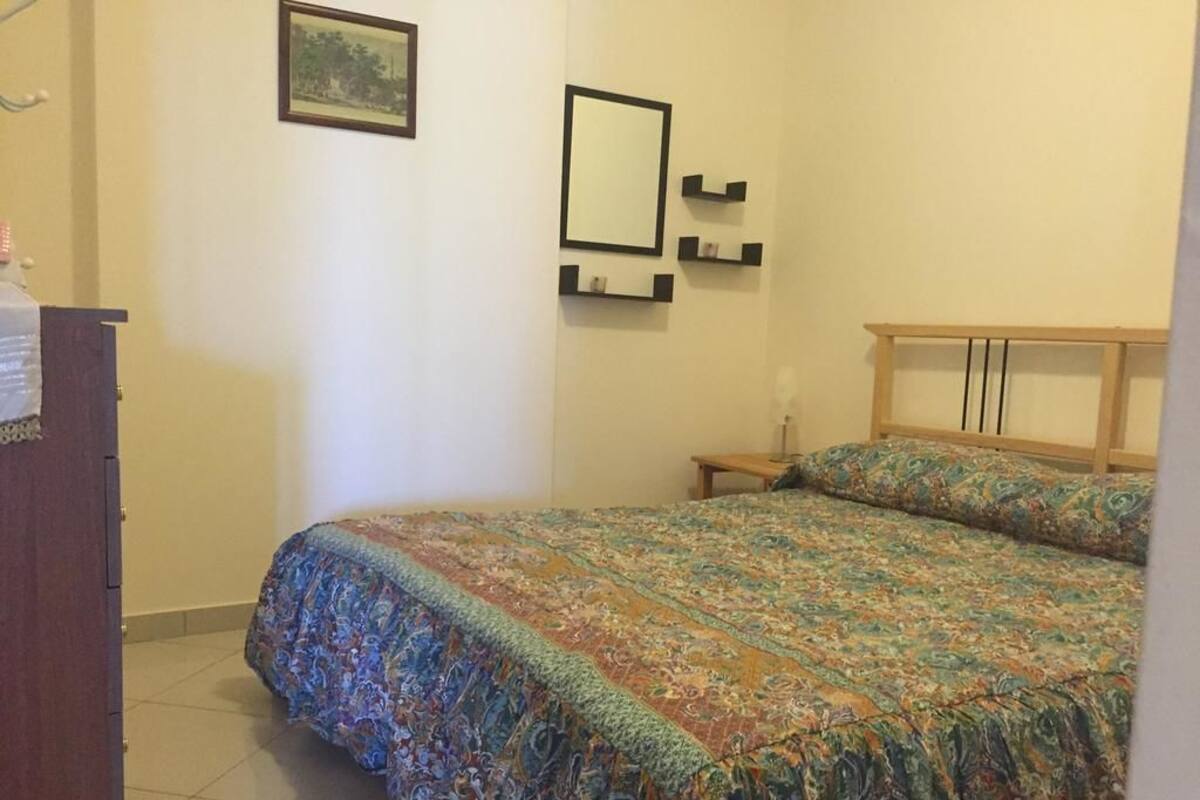 Un dormitorio con cama, cabecera de madera, mesita de noche, cómoda y un cuadro en la pared.