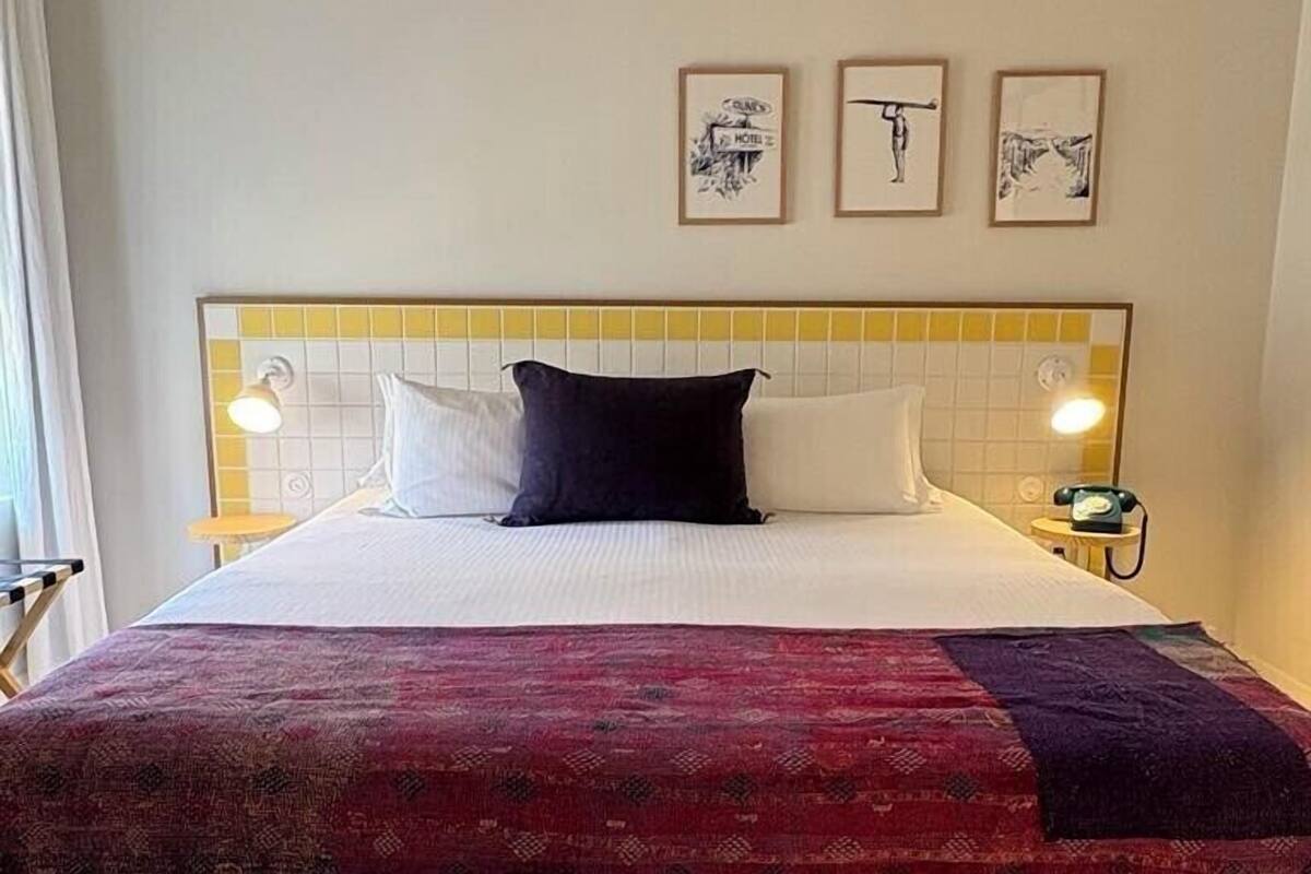 A hotel room with a bed, two bedside lamps, a telephone, and three framed pictures on the wall.
