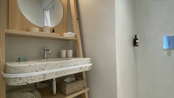 Un baño moderno con un mueble de tocador de madera independiente, un espejo redondo, ducha con piso de azulejos y un perchero para toallas.