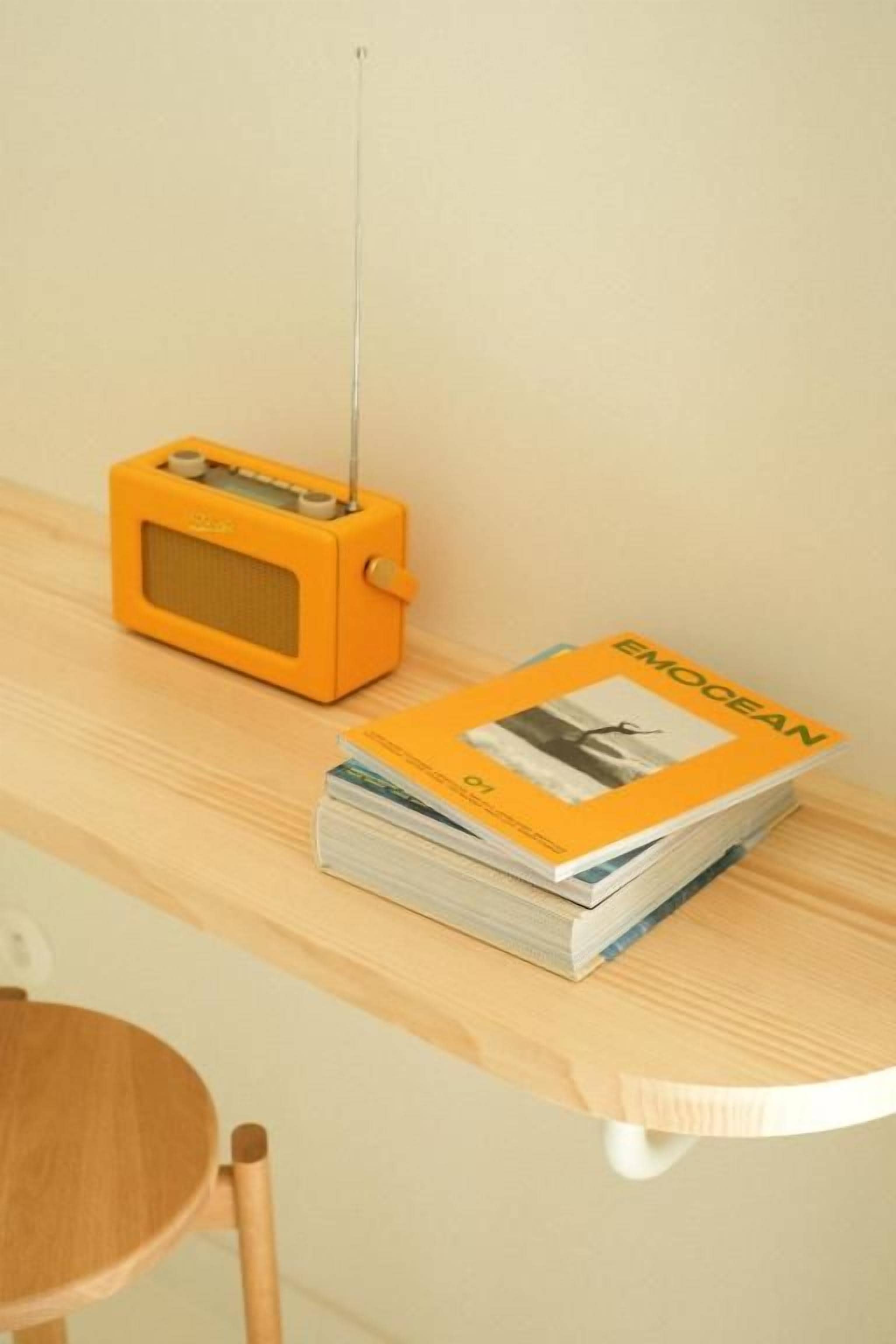 Una radio pequeña naranja sobre una repisa de madera, con una revista titulada 'OCEAN' a su lado.