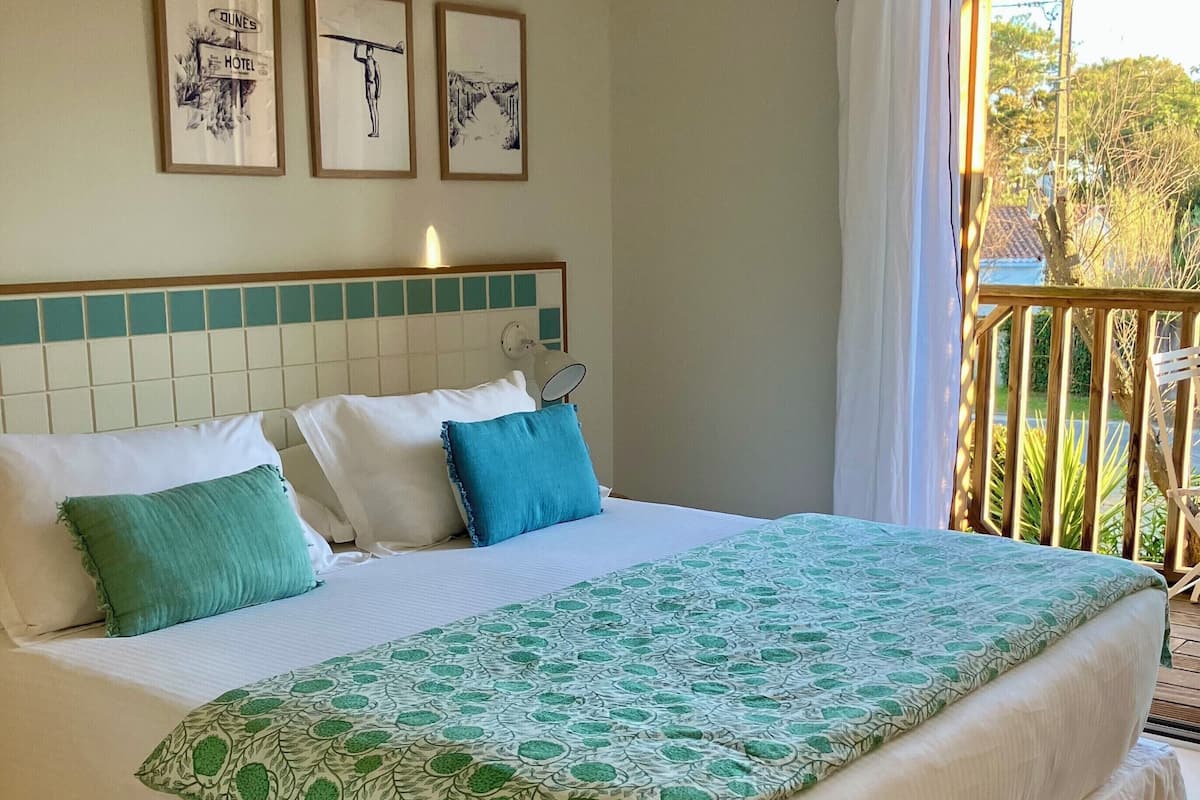 A neatly made bed with a green and white patterned bedspread, white pillows, and a teal accent pillow. There are three framed pictures on the wall above the bed.