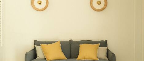 A living room with a grey sofa, two yellow cushions, and two wicker chairs around a small wooden table.