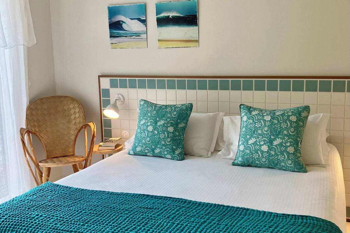 A hotel room with a bed, two pillows, a chair, a nightstand, and two wall art pieces.
