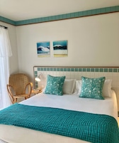 Habitación de hotel con cama, dos almohadas, una silla, una mesita de noche y dos cuadros en la pared.