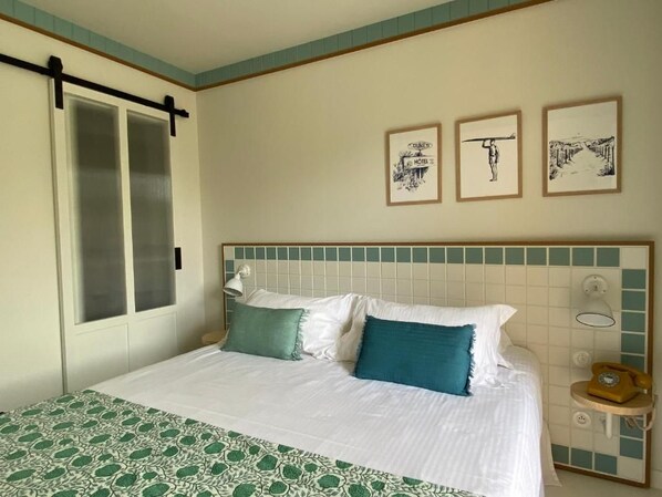 Habitación de hotel con cama, mesita de noche, teléfono y tres cuadros en la pared.