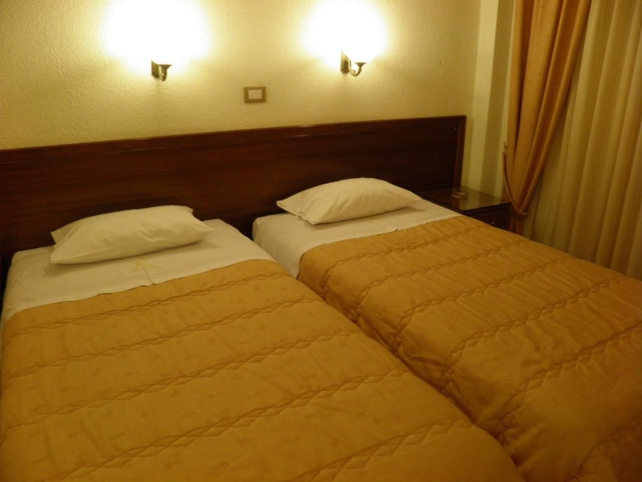 A hotel room with two beds, each with a headboard and pillows, and two wall-mounted light fixtures.