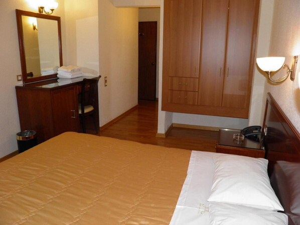 A hotel room with a bed, a dresser, a mirror, a wardrobe, and a bedside table with a lamp.