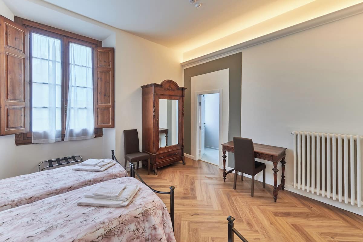 A hotel room with two beds, a wooden desk, a chair, a large mirror, and a radiator.