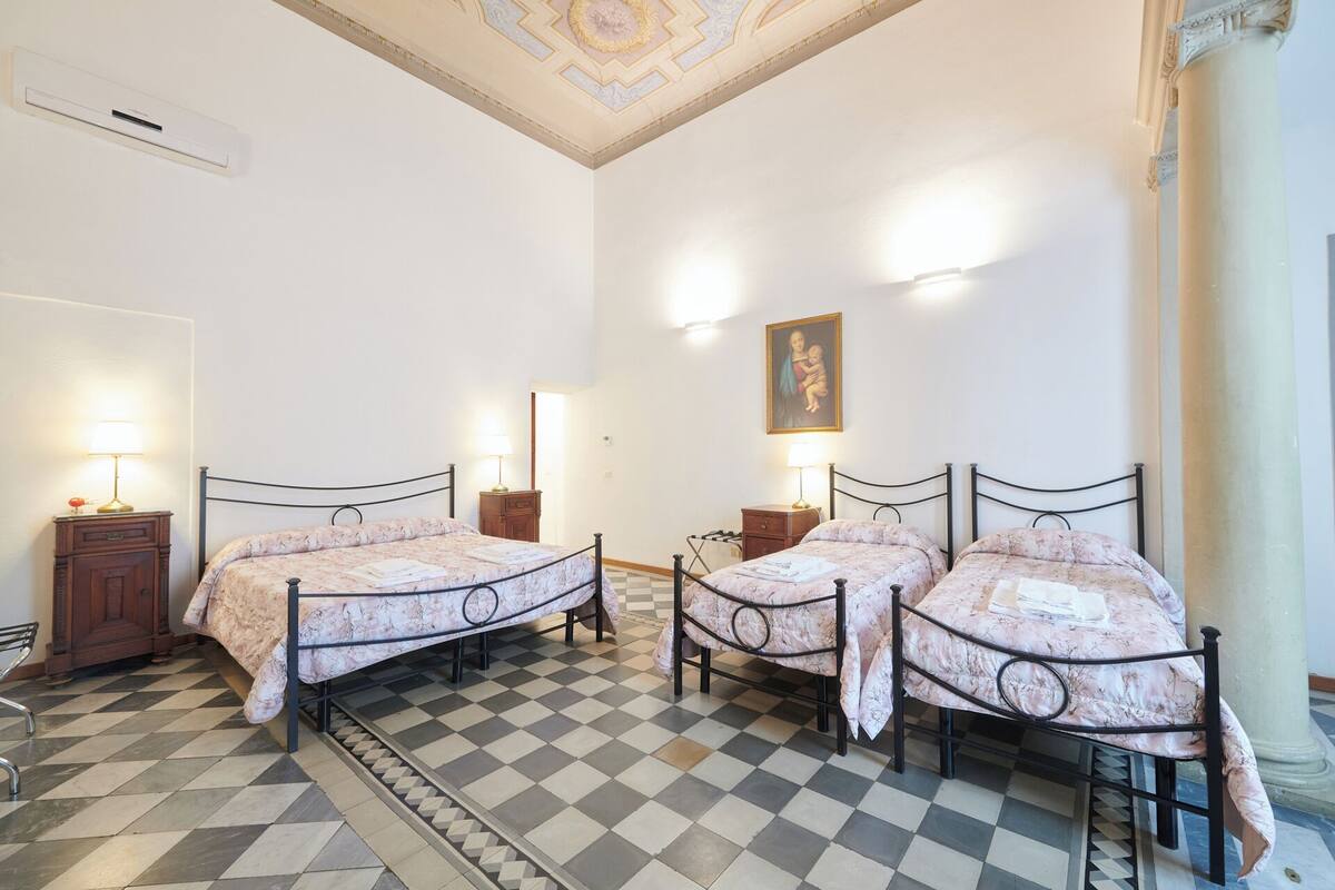 A room with two beds, a checkered floor, a painting on the wall, and a ceiling with a decorative pattern.