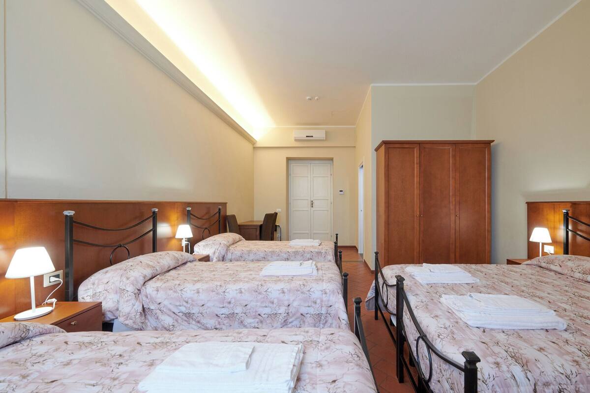A hotel room with three beds, each with a headboard and bedside table, a wardrobe, and a door leading to another room.