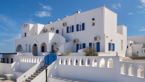 Un edifici blanc amb persianes blaves, una escala i un cel blau clar.