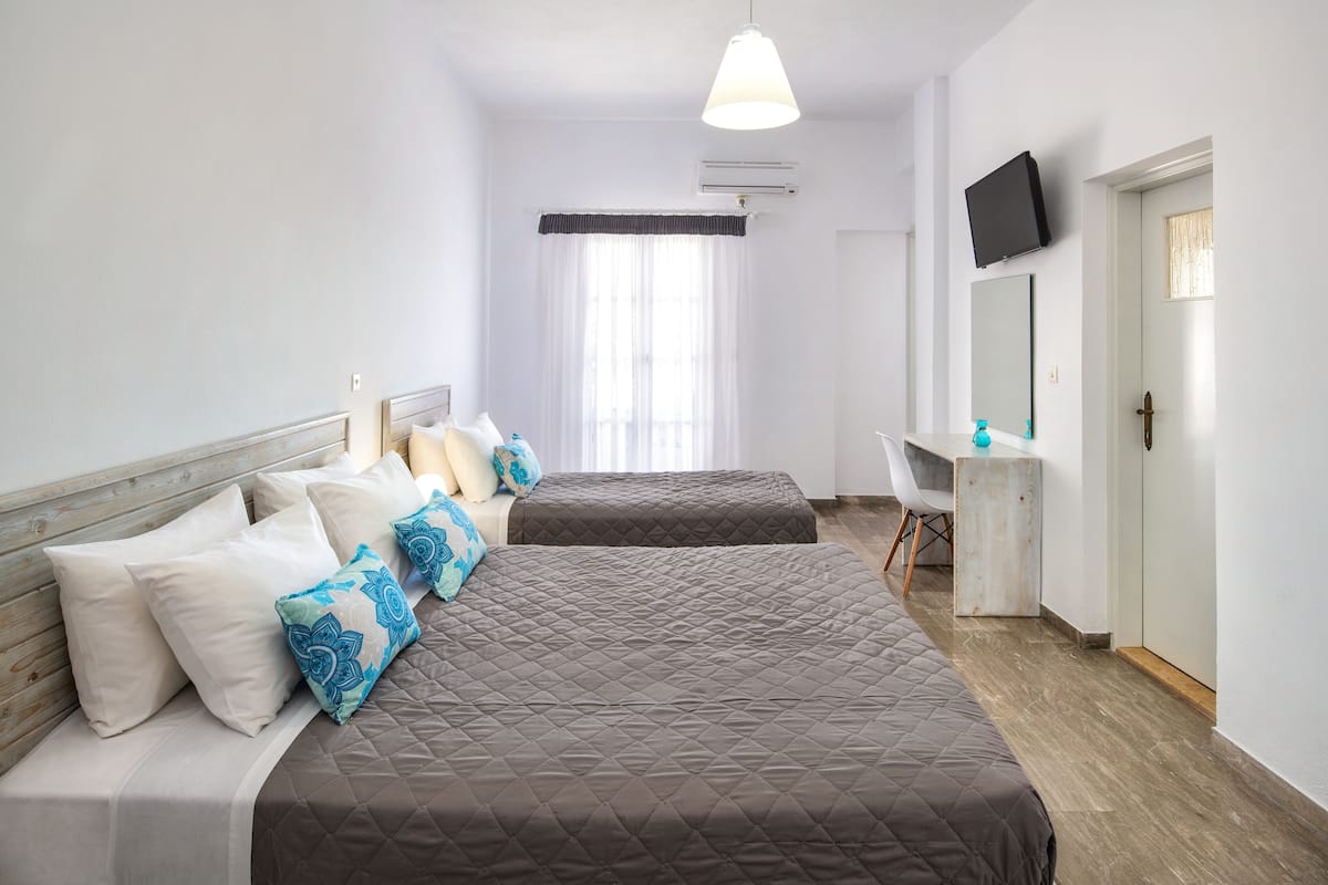 A hotel room with two beds, a desk, a chair, a TV, and a window with curtains.