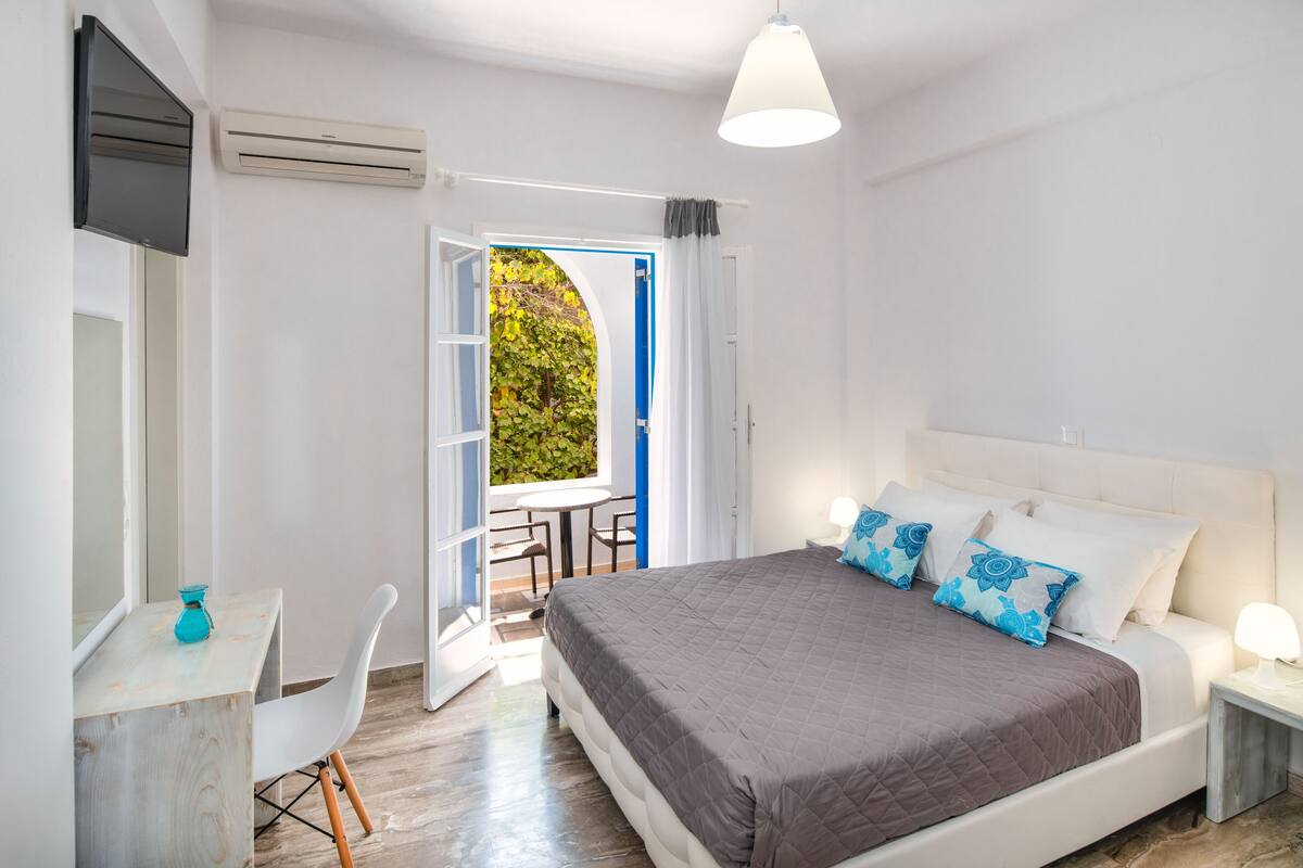A bedroom with a bed, bedside tables, a desk, and an open door leading to a balcony.