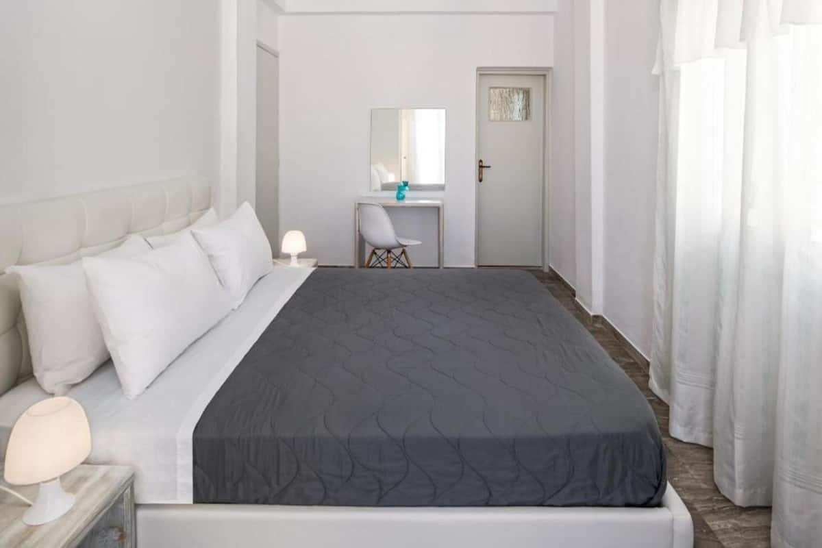A bedroom with a bed, a desk, a chair, and a door.