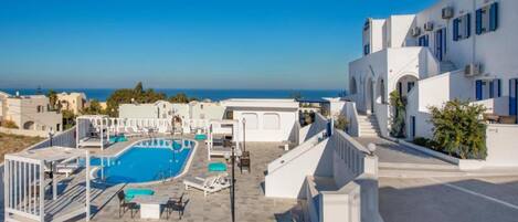 Zona de piscina en la azotea con vistas despejadas al mar, edificios blancos con contraventanas azules y una escalera que conduce a los pisos superiores.