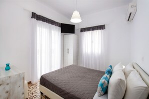 A bedroom with a bed, curtains, a wardrobe, and a ceiling fan. - Villa Kavallaris & Apartments (Santorini)