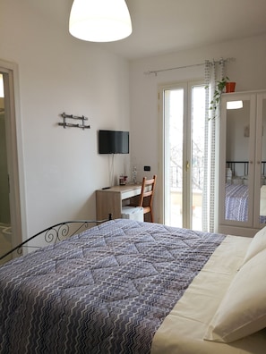 A bedroom with a bed, a desk, a chair, a TV, and a sliding door to a balcony. - B&B Il Papavero Rosso (Corigliano D'Otranto)