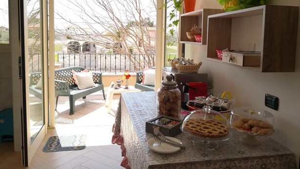 A kitchen with a view of the street, a dining table with food, and a counter with kitchen items.