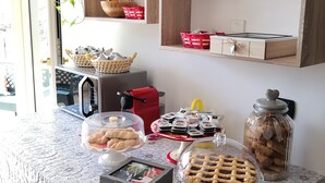 A breakfast table with various food items, a coffee machine, and a red bag.