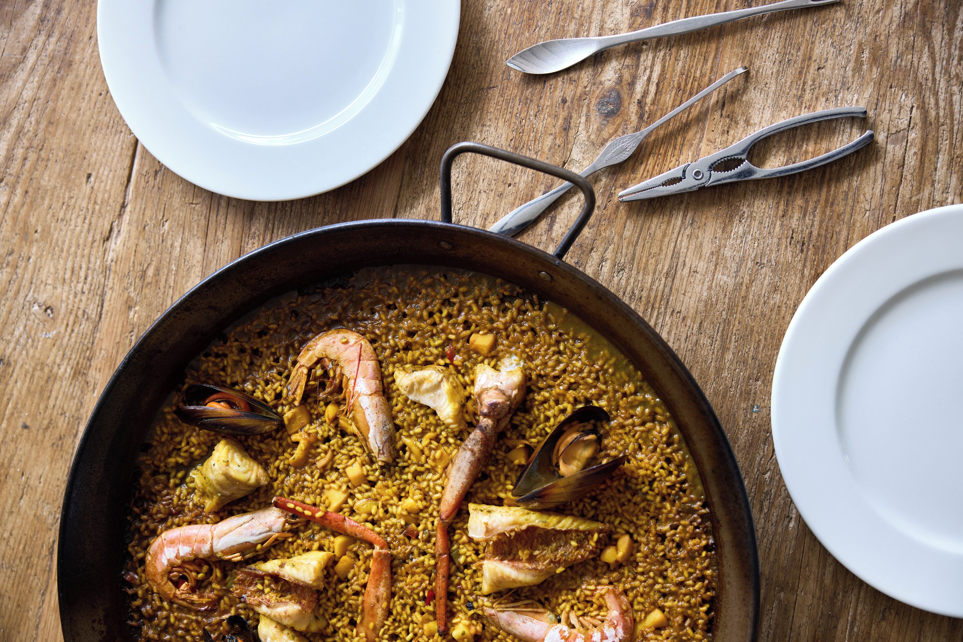 Eine große Pfanne mit Meeresfrüchte-Paella auf einem Holztisch.