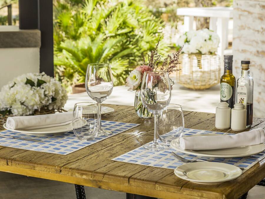Una mesa de madera dispuesta con platos blancos, copas transparentes y una botella de vino Santa Oliva.