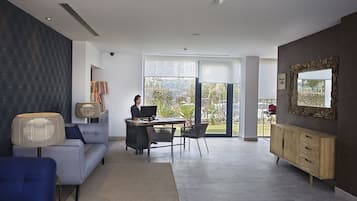 A modern living room with a sofa, a desk, and a computer. There is a large window with a view of greenery outside.