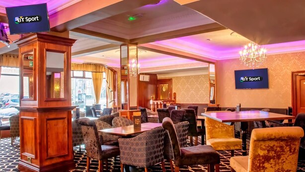 A hotel lobby with a large wooden desk, patterned chairs, and a chandelier. - The Revelstoke Hotel (Bridlington)
