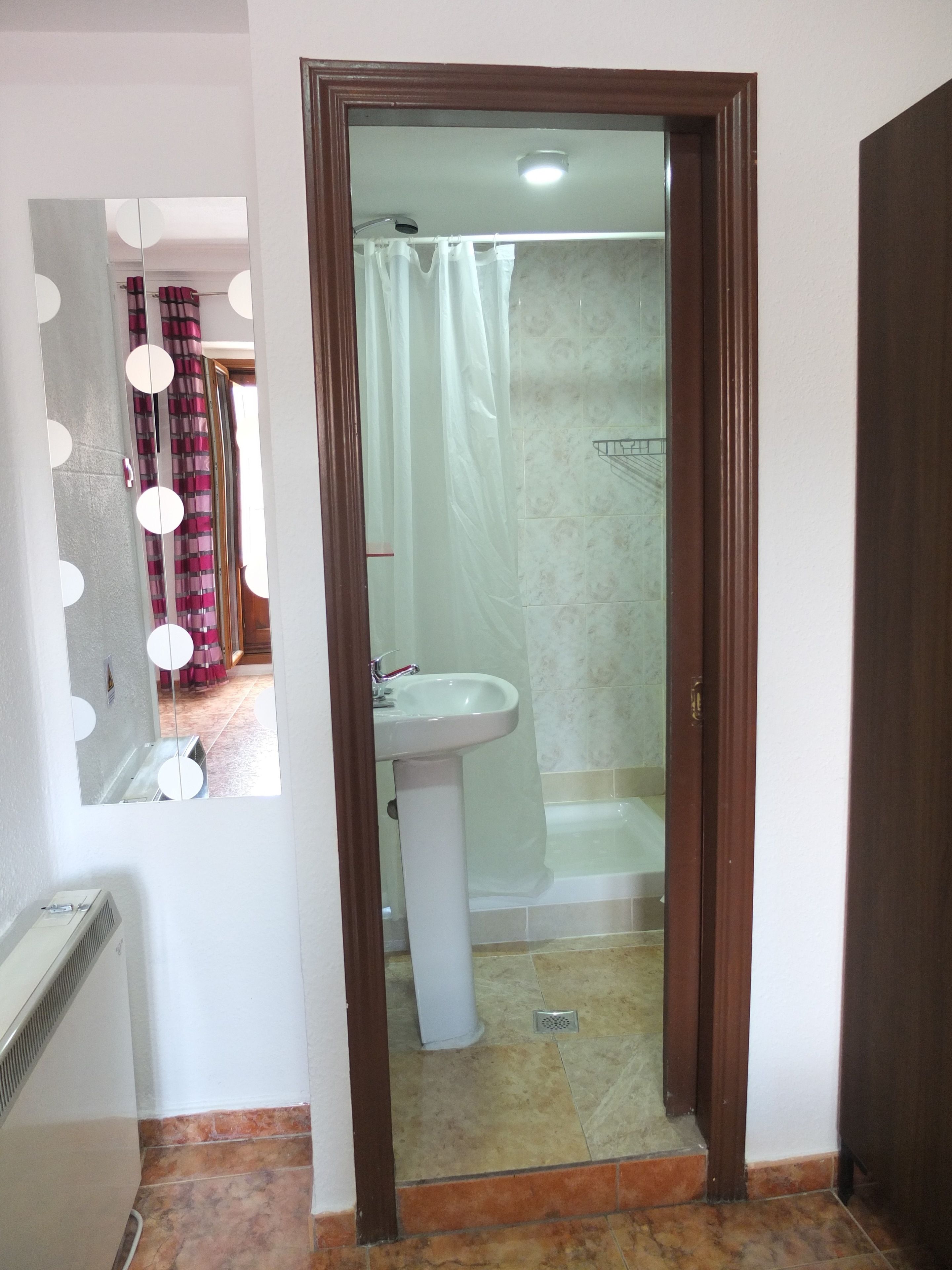 Un baño con un lavamanos blanco, ducha y espejo con iluminación.