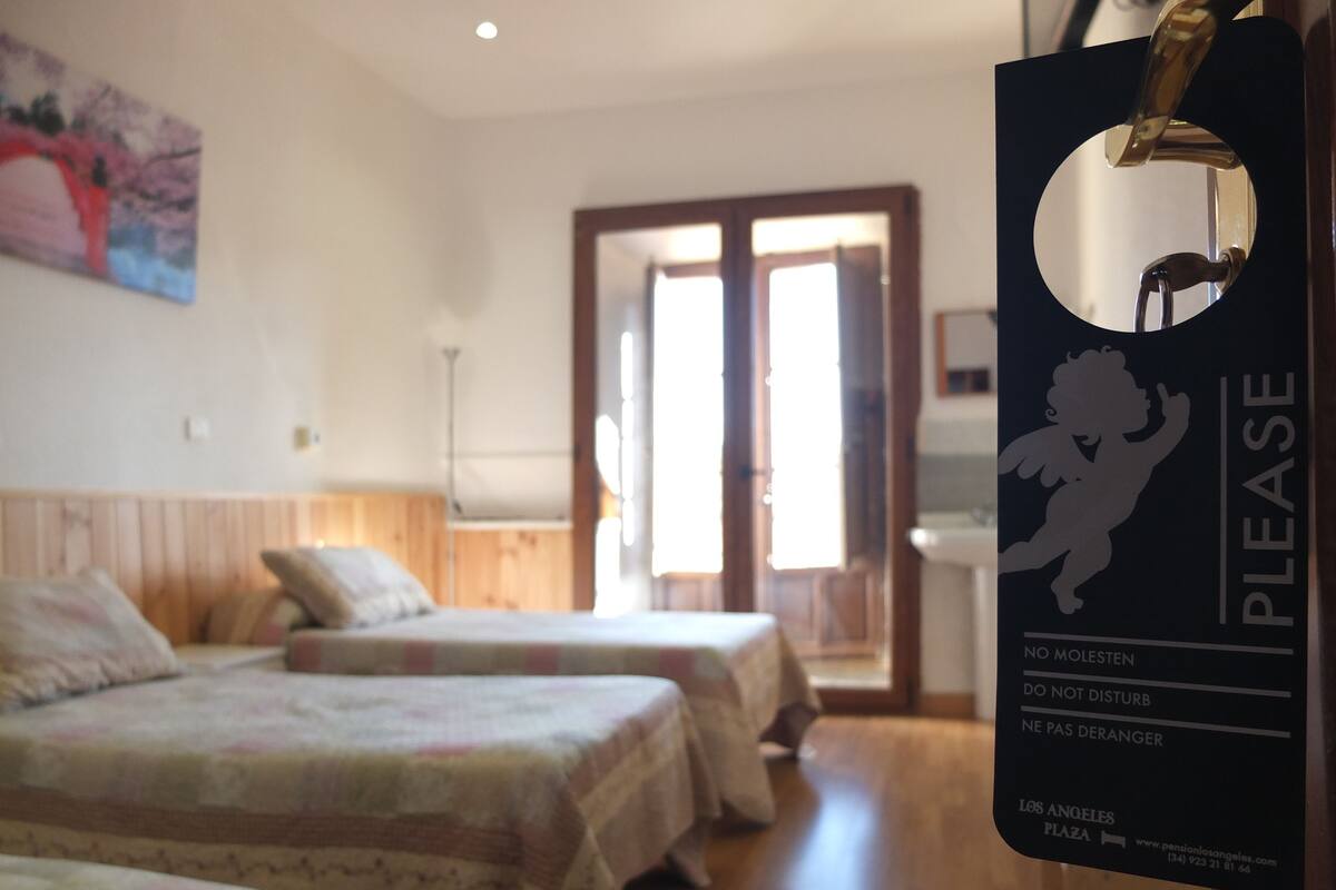 Une chambre d’hôtel avec deux lits, un tableau au mur et une pancarte indiquant « Veuillez ne pas déranger ».