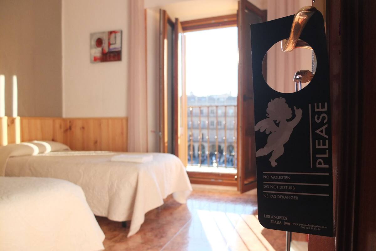 Une chambre d’hôtel avec deux lits, un plancher en bois et une vue sur la place de Los Angeles. Une pancarte sur la porte indique : « VEUILLEZ NE PAS FAIRE DE TAPAGE, NE PAS DÉRANGER. »