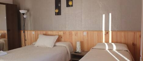 A hotel room with two beds, a bedside table with a lamp, and three wall art pieces.